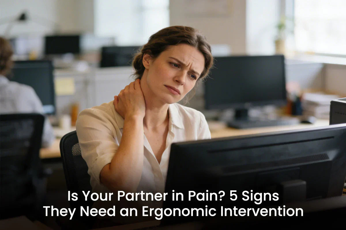 A woman at an office desk grimaces while rubbing her neck in pain, looking at a computer monitor, with the text overlay: 'Is Your Partner in Pain? 5 Signs They Need an Ergonomic Intervention'