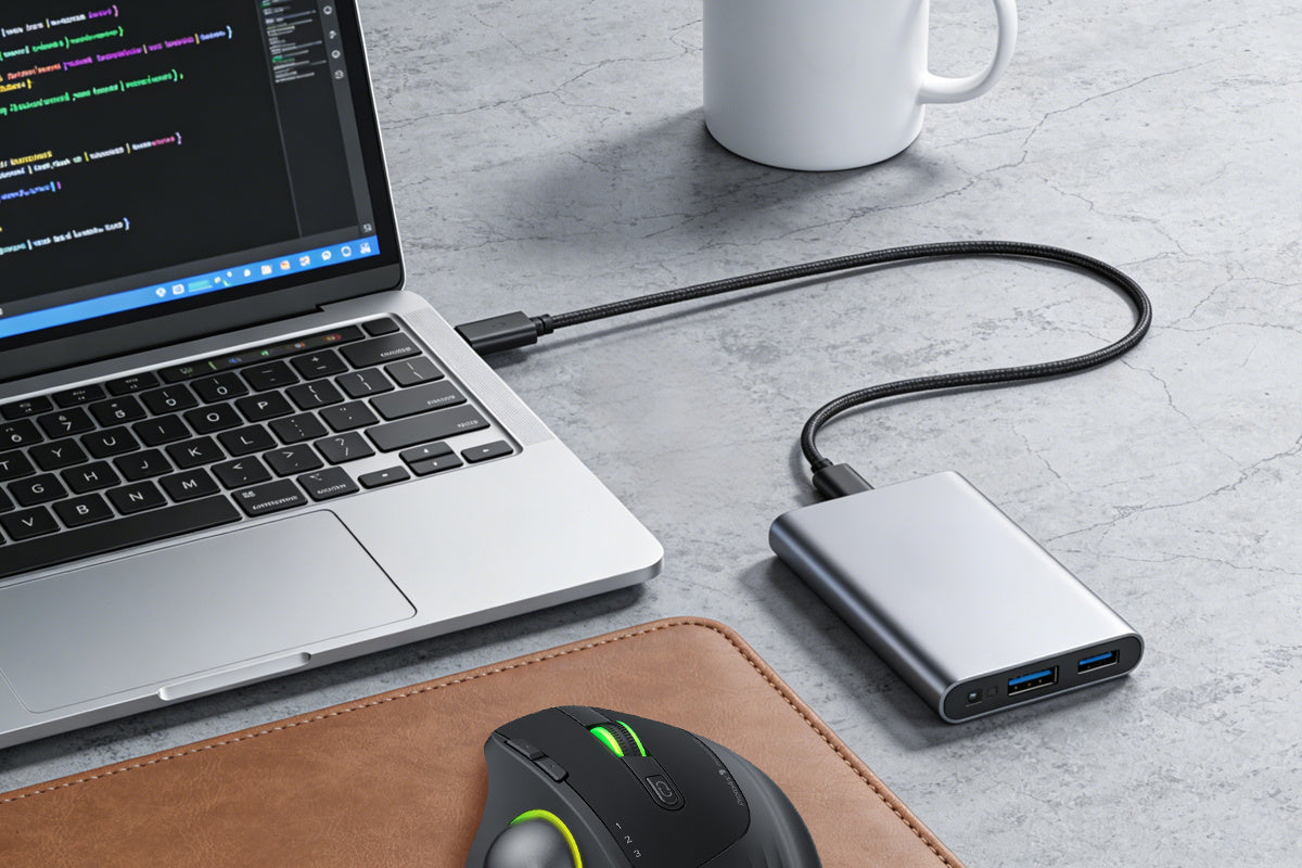 Laptop workstation with USB-C hub, gaming mouse on leather mousepad, and coffee mug on concrete desk surface, showing coding environment