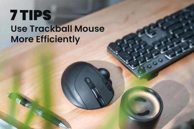A black trackball mouse on a wooden desk with a keyboard and coffee.