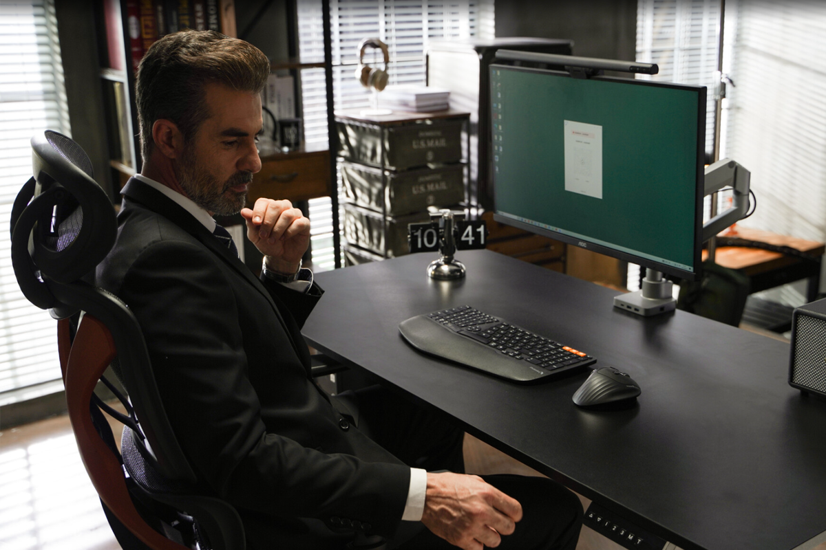A man in a suit sitting at a desk in an office, using a computer.