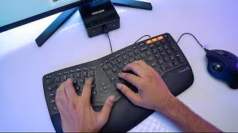 A person typing on a black ergonomic keyboard with a trackball mouse on the desk.
