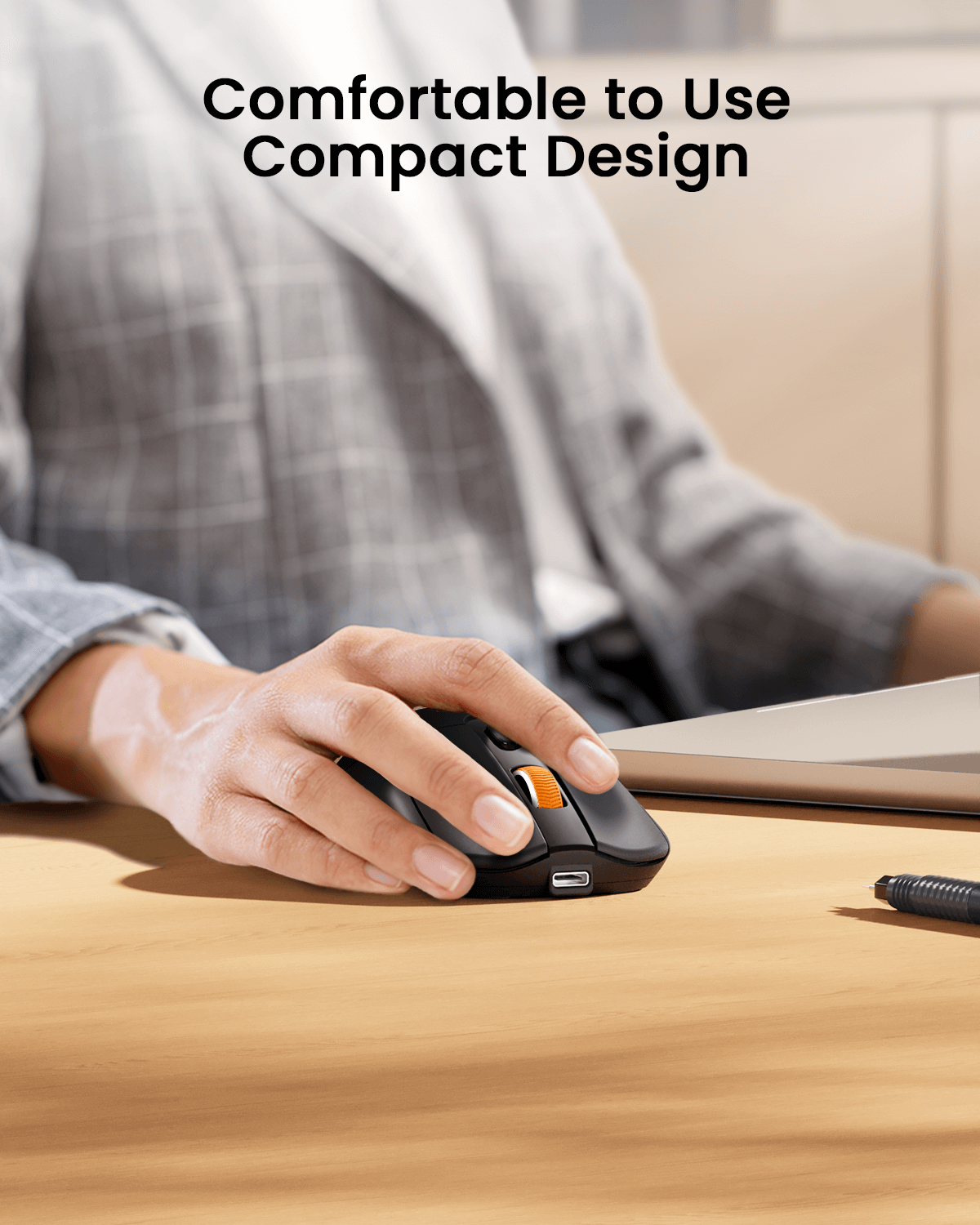 Black EM15 wireless mouse with orange scroll wheel being held by a hand on a wooden desk, highlighting ergonomic comfort.